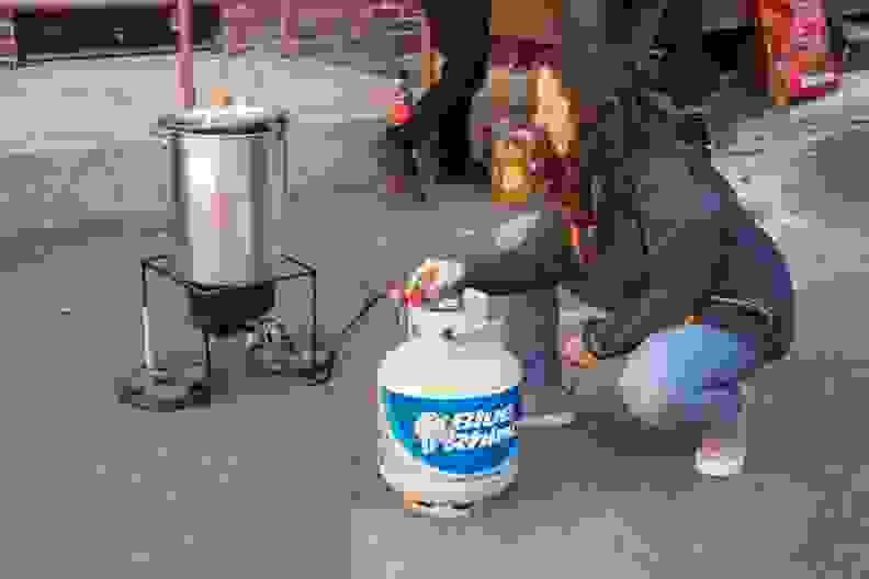 A person adjusts the propane tank connected to an outdoor deep fryer.