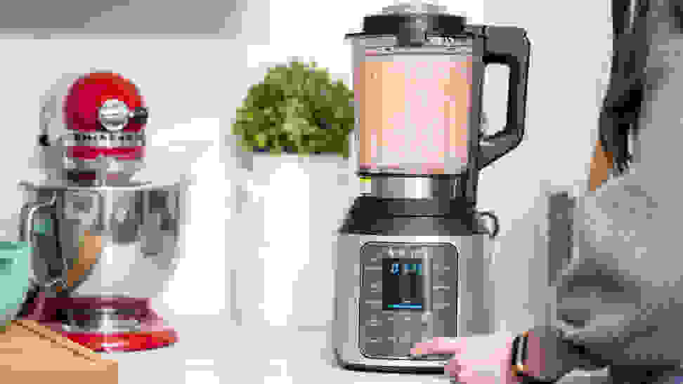 A person blends a smoothie in a blender on a countertop surrounded by other kitchen items.