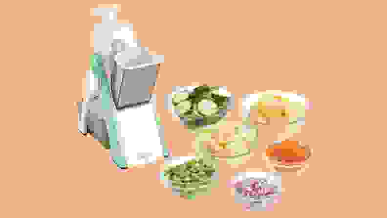 Dash Mandoline surrounded by bowls of sliced vegetables on an orange background