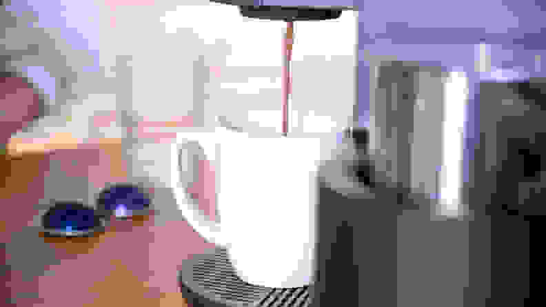 A white mug of coffee under a Keurig coffee maker