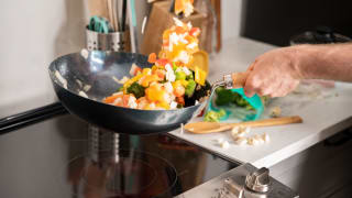 A person is stir frying a medley of vegetables in a carbon steel wok over an electric cooktop.