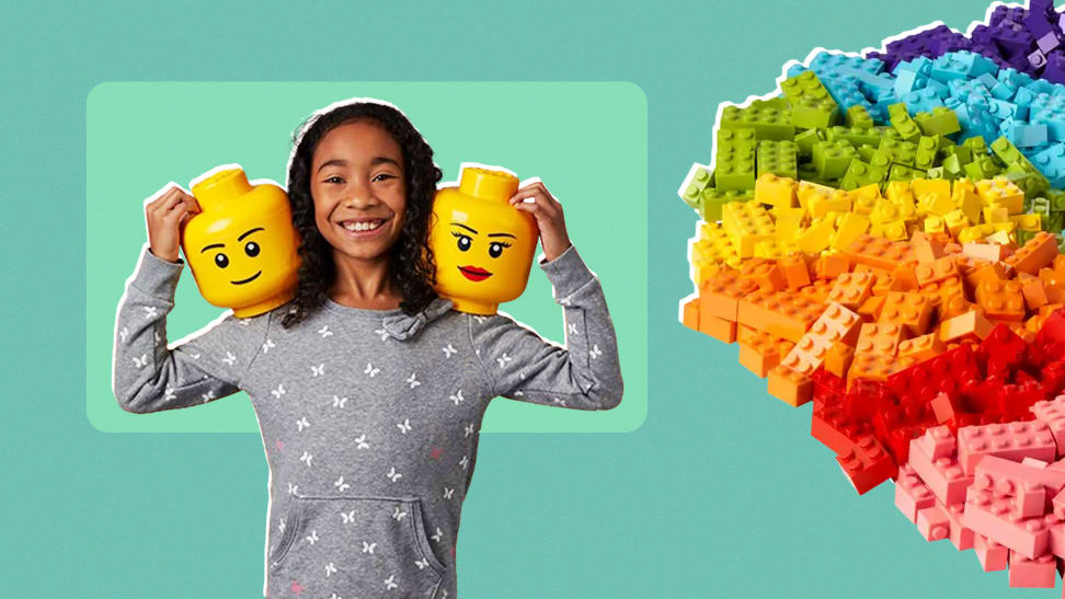 A girl holding two Lego heads on her shoulders next to a rainbow-colored pile of Legos.