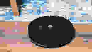 The iRobot Roomba Comobo Essential on a hardwood floor next to carpet.