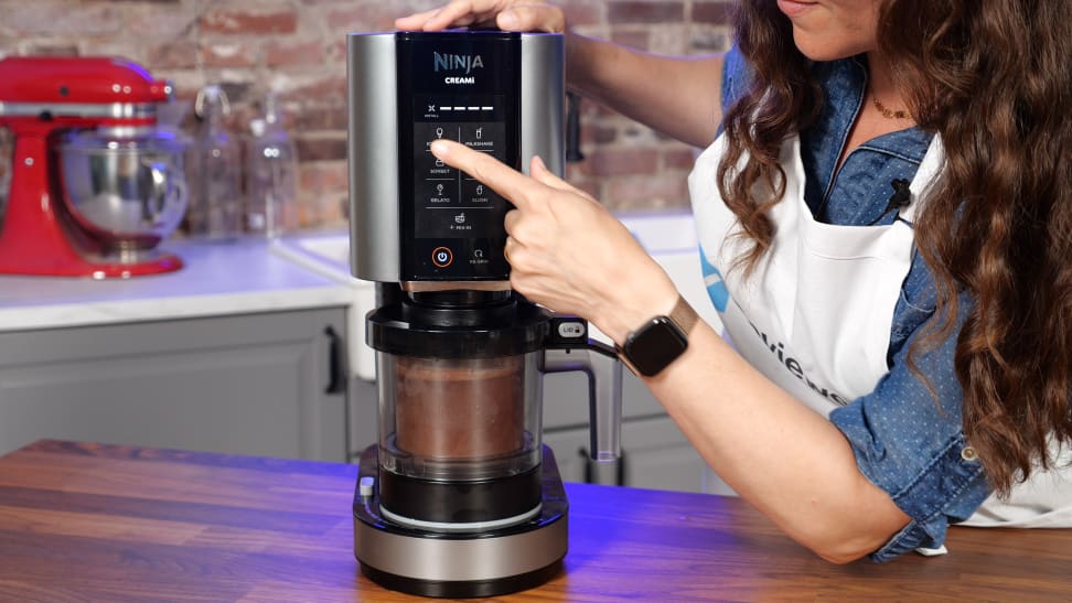 A person pressing a button on the Ninja Creami ice cream maker, with chocolate ice cream in the pint container.