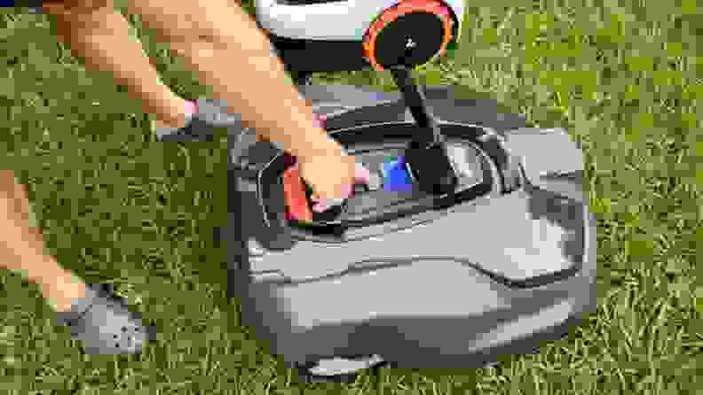 A person entering a passcode on the top of a robot lawn mower