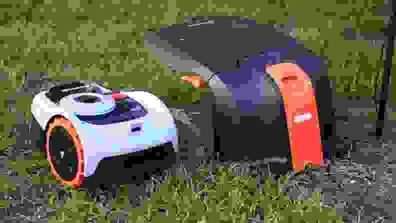 The Segway Navimow robot lawn mower sits in the grass next to it's base station