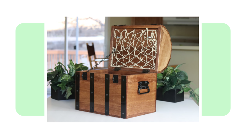 A small wooden treasure chest with the lid opened in front of light green background.