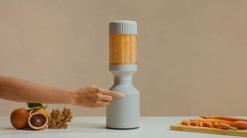 A person using their finger to power on the Beast blender to mix a carrot and orange smoothie.