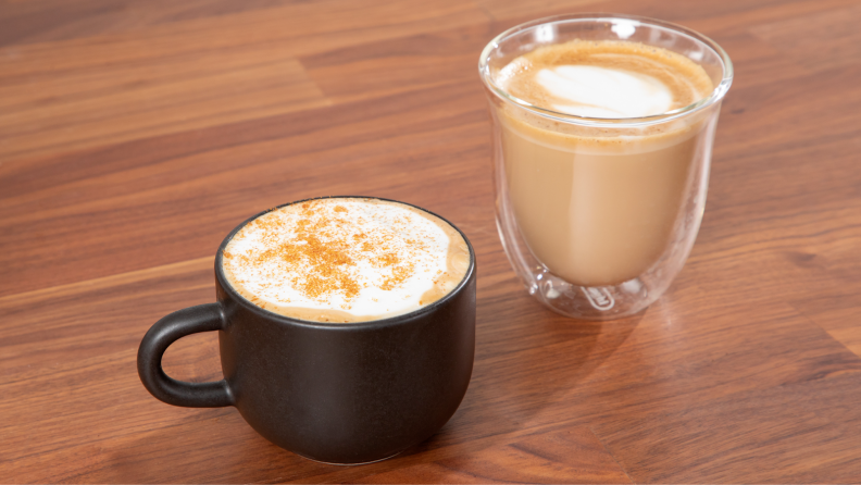 Two cups of espresso coffee on top of wooden countertop surface.