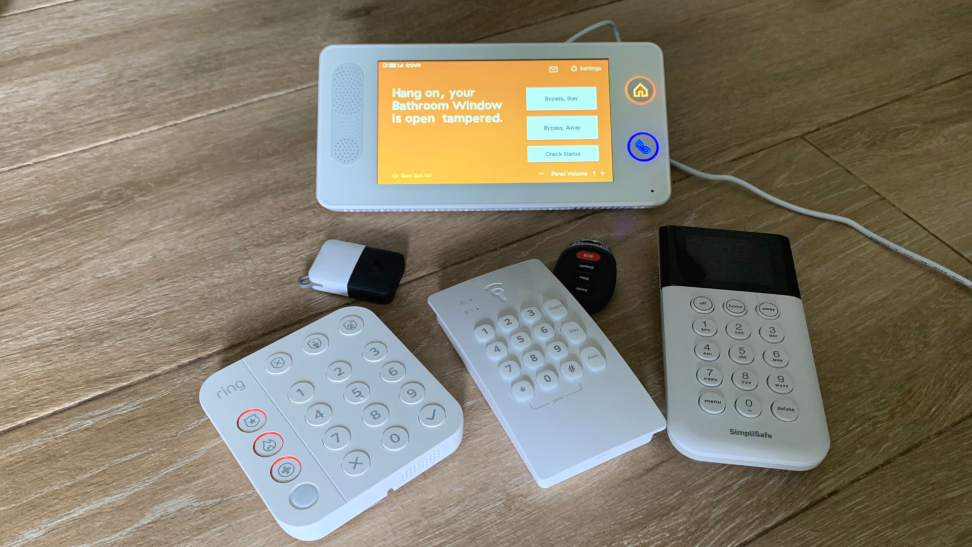 Home security system panels, keypads, and keyfobs scattered on a tile floor.