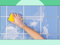 A hand wearing a glove washes a tiled wall with a sponge.