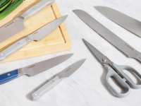 Misen knife set is spread on a marble counter and wood cutting board with scallions in the background.