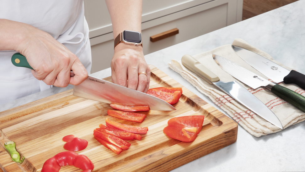 Hand cutting a bell pepper with a chef's knife, beside a line of other chef's knives.