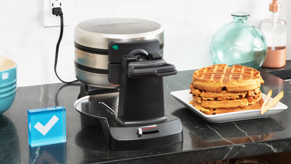 The Cuisinart Double Flip Belgian Waffle Maker sits on a black counter with a stack of waffles to the right, and the Reviewed logo to the left.