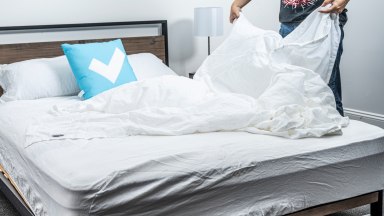 A person standing at a bed, holding some white sheets.