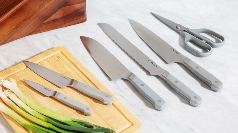 Misen knife set laid out on a marble countertop beside a cutting board of scallions