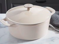 Product shot of the cream colored Made In Dutch Oven with lid on top of granite countertop next to gray dishcloths.