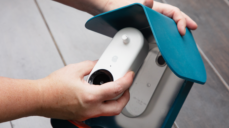 A person's hand moves a white camera into a slot on a Bird Buddy bird house.