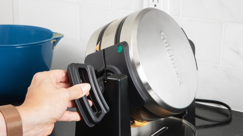 A person turning the handle of the Cuisinart Double Flip Belgian Waffle Maker.