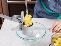 Cubed potatoes in a potato ricer over a glass bowl