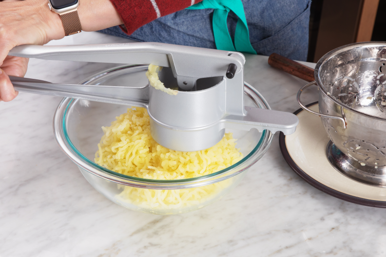 Squished potatoes coming out of a potato ricer into a glass bowl