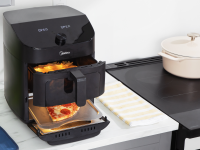 Midea air fryer on a kitchen counter with pizza cooking in bottom section and fries cooking in top basket