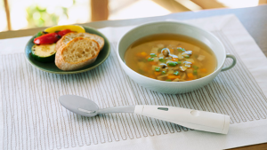 The Kirin Electric Spoon sits on a placemat in front of a bowl of soup and a plate of bread.