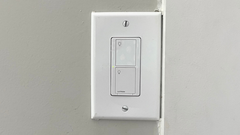 The Lutron Caséta Smart Light Switch hangs on a wall.