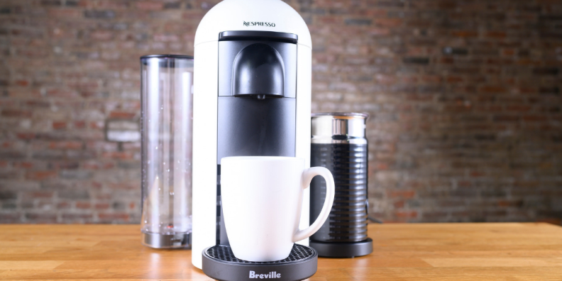 Nespresso VertuoPlus by Breville on a wooden surface, with a white mug underneath