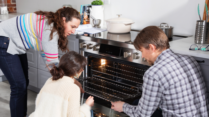 Three people gather around a range with the door open.