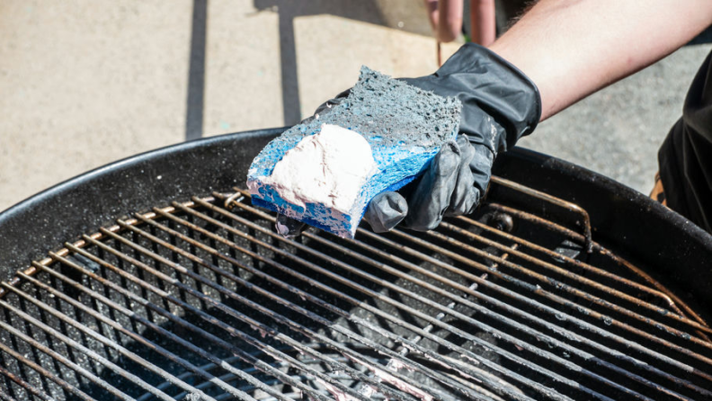 A Scotch-Brite Zero-Scratch sponge is shown with The Pink Stuff paste on it over a grill for cleaning.