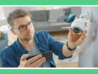 Person adjusting mounted smart security camera on wall indoors while holding smartphone.